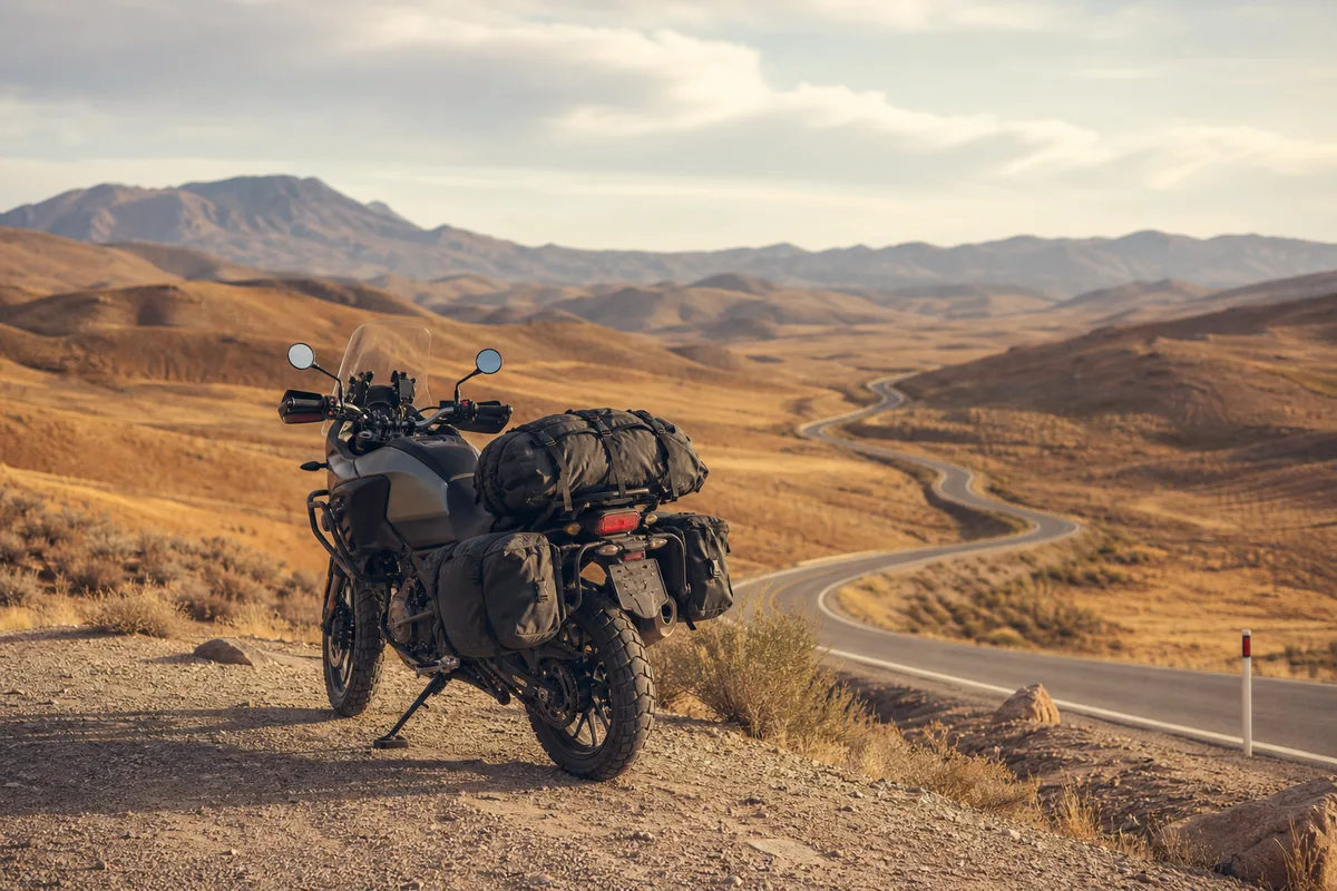 Sacoches de voyage sanglées sur un trail routier, garé seul face à une route sinueuse traversant un paysage aride